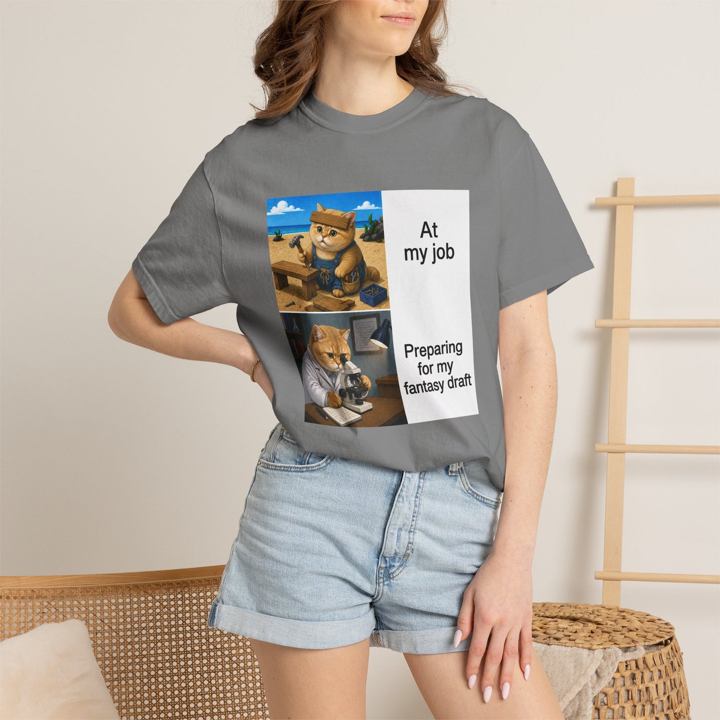 Grey Comfort Colors 1717 t-shirt with a square two-panel print on an off-white card across the chest: an orange cat in denim overalls hammering a nail into a wooden bench on a beach, captioned At my job, above the same cat in a white lab coat hunched over a microscope beside a notebook of stats, captioned Preparing for my fantasy draft.