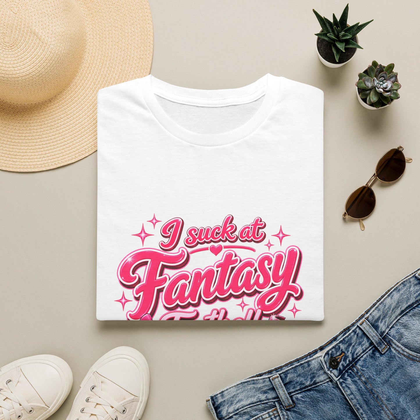 Gildan 64000 Softstyle t-shirt folded, showing the pink script I suck at Fantasy Football print with a bow-tied football and a shattered trophy.