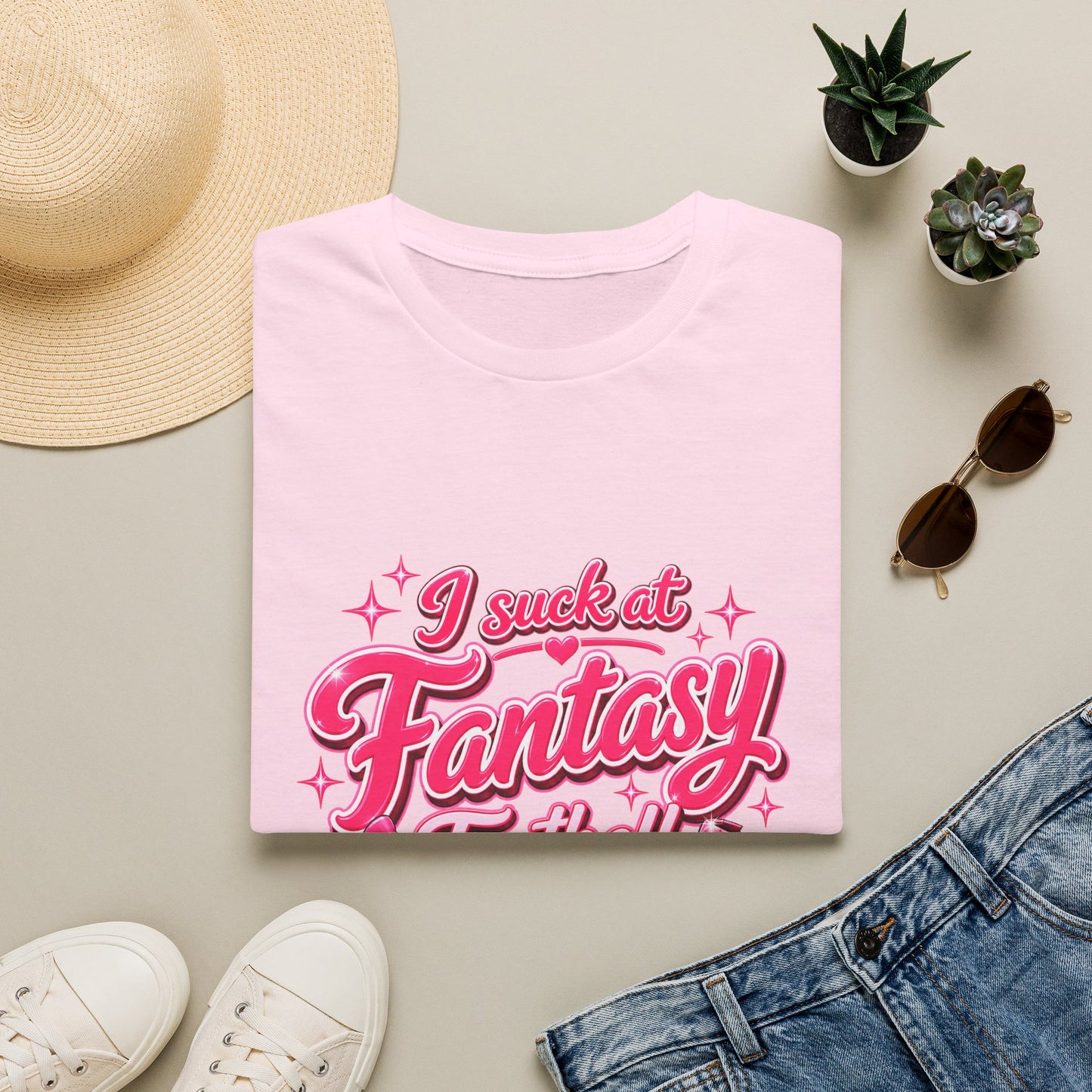 Gildan 64000 Softstyle t-shirt folded, showing the pink script I suck at Fantasy Football print with a bow-tied football and a shattered trophy.