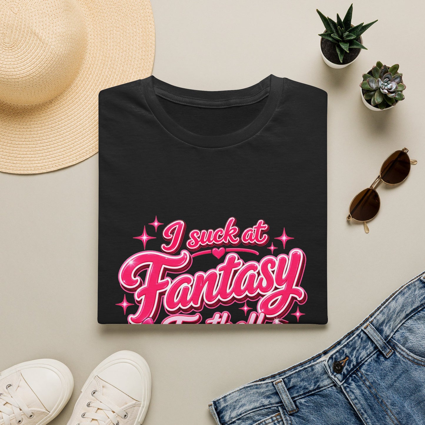 Gildan 64000 Softstyle t-shirt folded, showing the pink script I suck at Fantasy Football print with a bow-tied football and a shattered trophy.