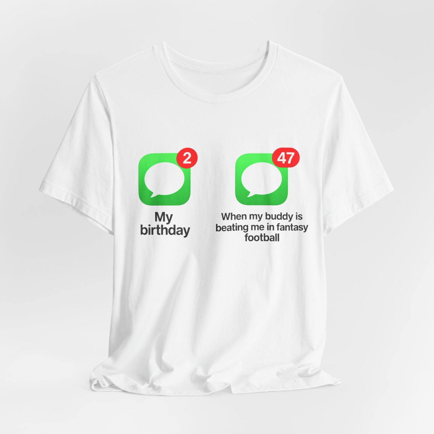White Bella+Canvas 3001 t-shirt printed across the chest with two green rounded-square icons, each holding a white speech bubble and a red notification badge, the left badge reading 2 above the caption My birthday and the right badge reading 47 above the caption When my buddy is beating me in fantasy football, in bold black lettering.