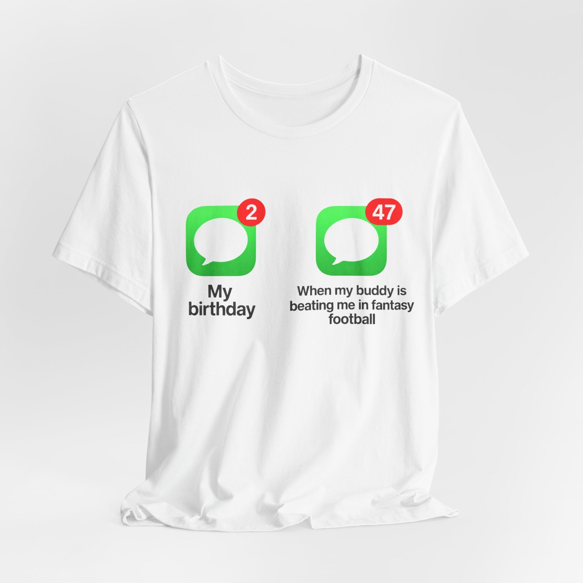 White Bella+Canvas 3001 t-shirt printed across the chest with two green rounded-square icons, each holding a white speech bubble and a red notification badge, the left badge reading 2 above the caption My birthday and the right badge reading 47 above the caption When my buddy is beating me in fantasy football, in bold black lettering.