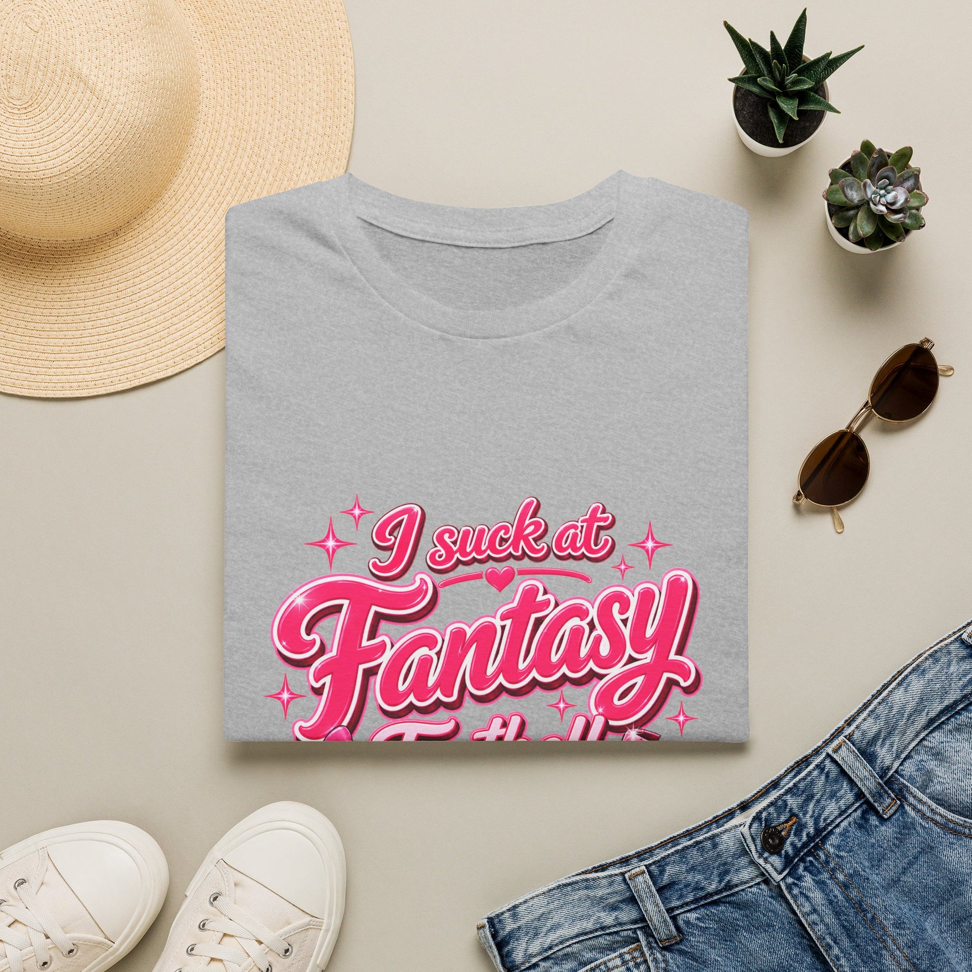 Gildan 64000 Softstyle t-shirt folded, showing the pink script I suck at Fantasy Football print with a bow-tied football and a shattered trophy.