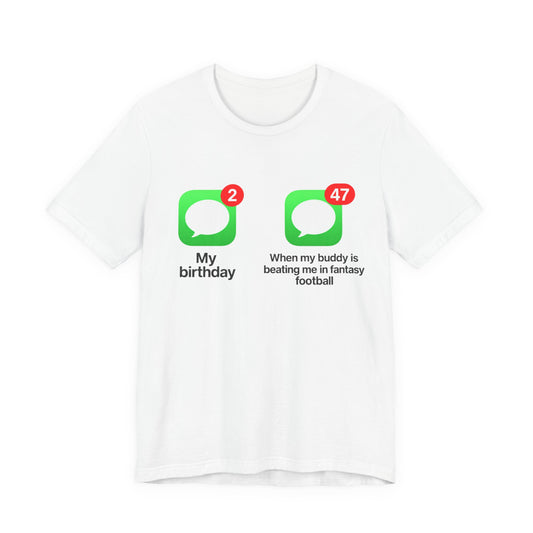 White Bella+Canvas 3001 t-shirt printed across the chest with two green rounded-square icons, each holding a white speech bubble and a red notification badge, the left badge reading 2 above the caption My birthday and the right badge reading 47 above the caption When my buddy is beating me in fantasy football, in bold black lettering.