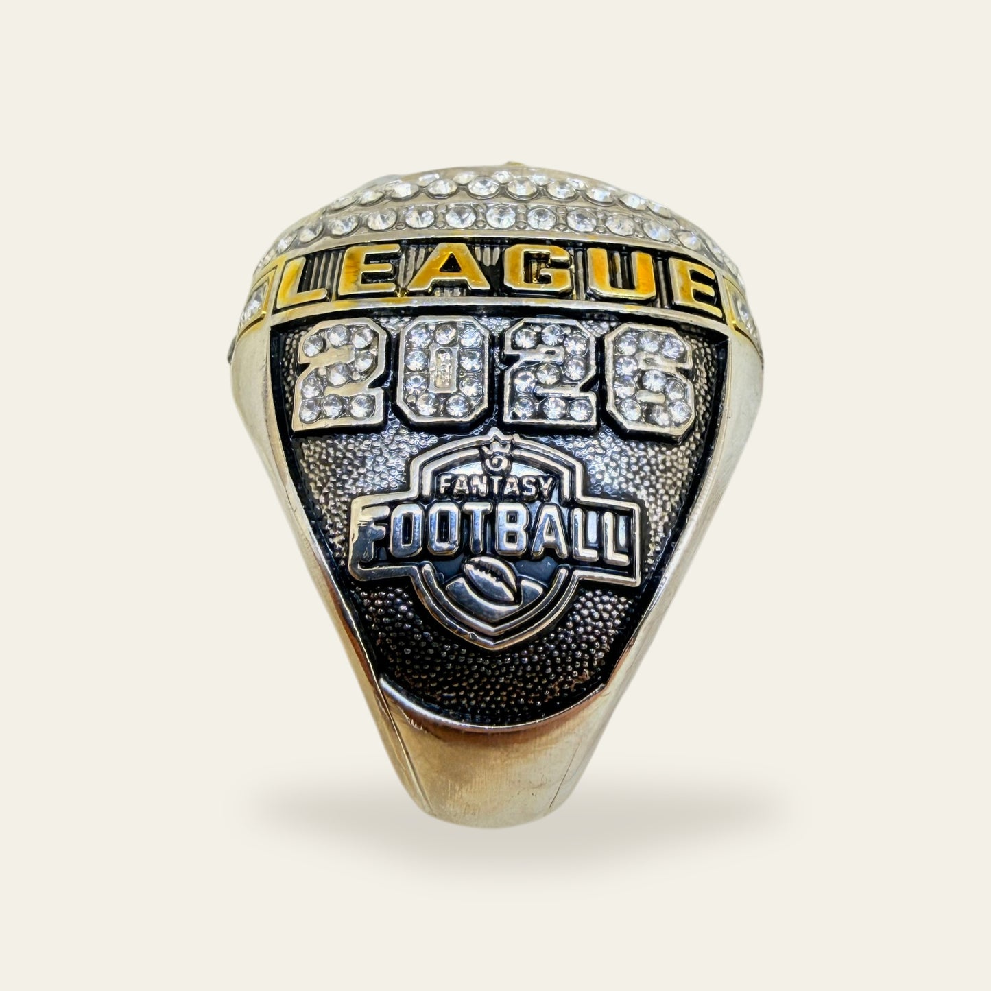 Black and white fantasy football championship ring, left shoulder view, with a gold LEAGUE rail, 2026 in clear stones, and a Fantasy Football shield on a black pebbled panel.
