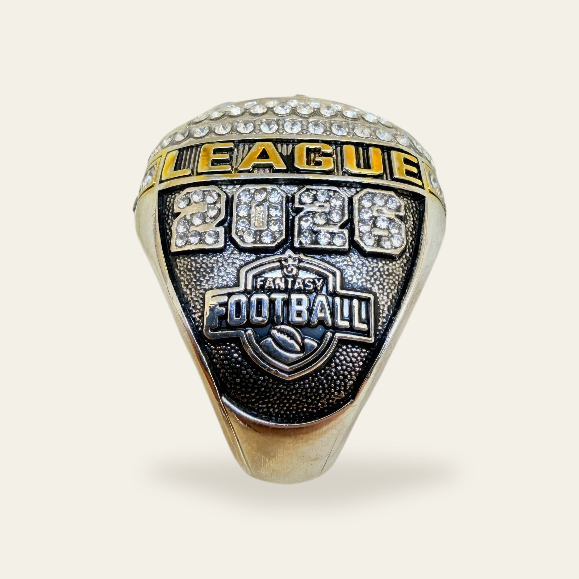 Black and white fantasy football championship ring, left shoulder view, with a gold LEAGUE rail, 2026 in clear stones, and a Fantasy Football shield on a black pebbled panel.