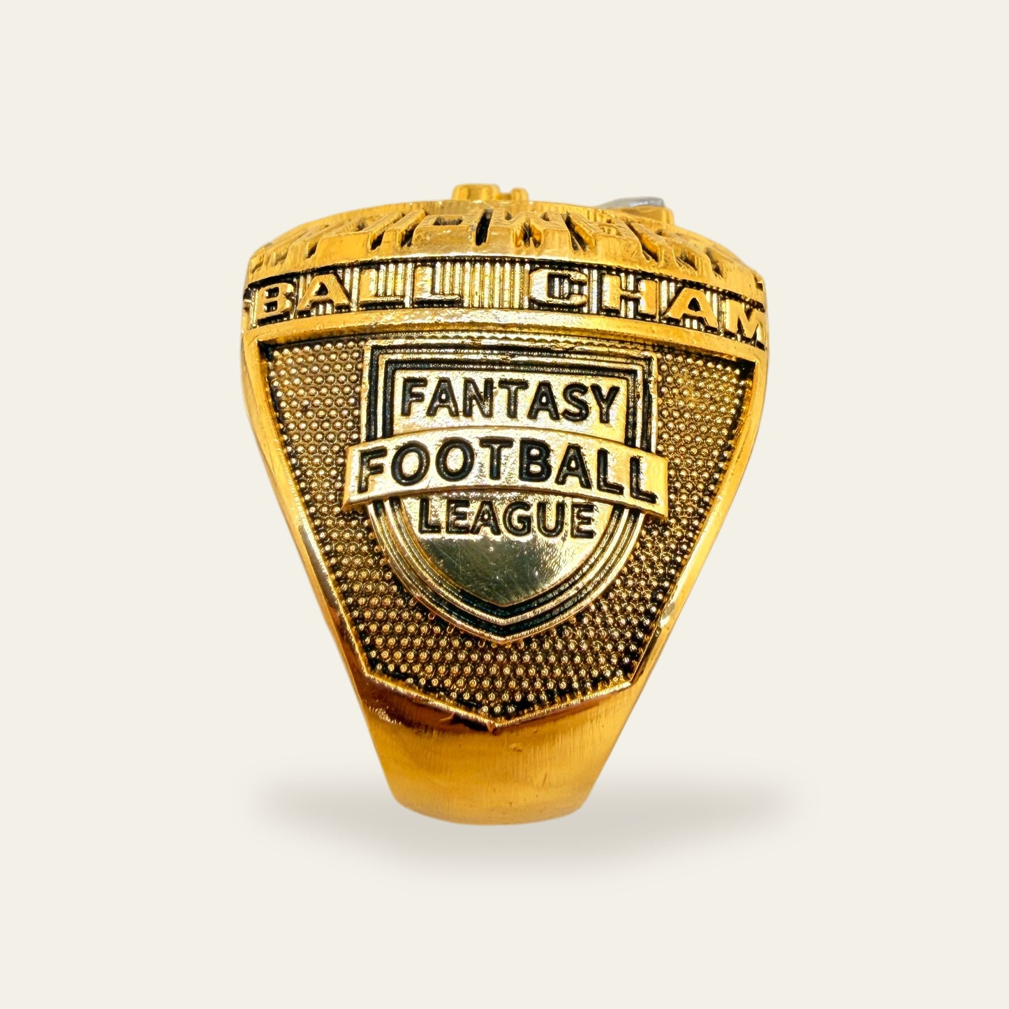 All gold fantasy football championship ring, right shoulder view, with a Fantasy Football League shield crest on a stippled gold panel under the lettered rail.