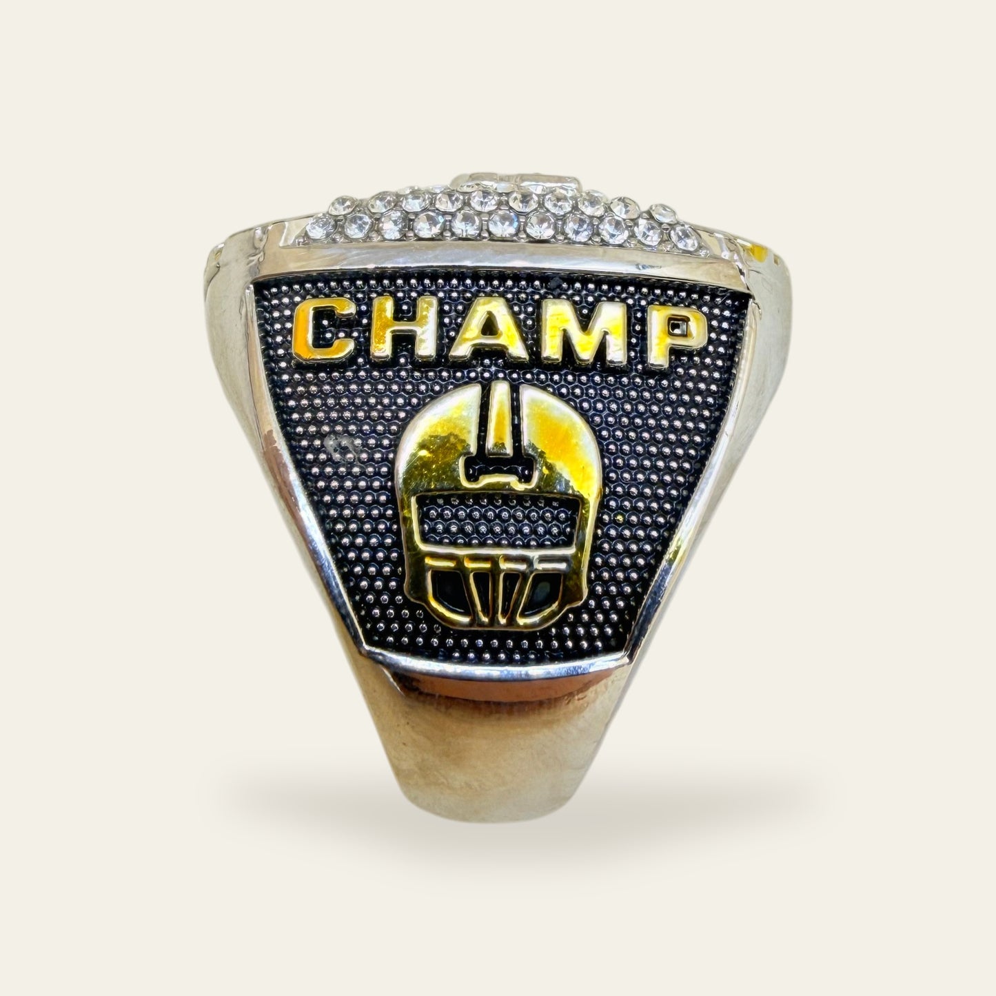 Two tone fantasy football championship ring, left shoulder view, with gold CHAMP letters above a gold football helmet on a black stippled panel, under a row of clear stones.