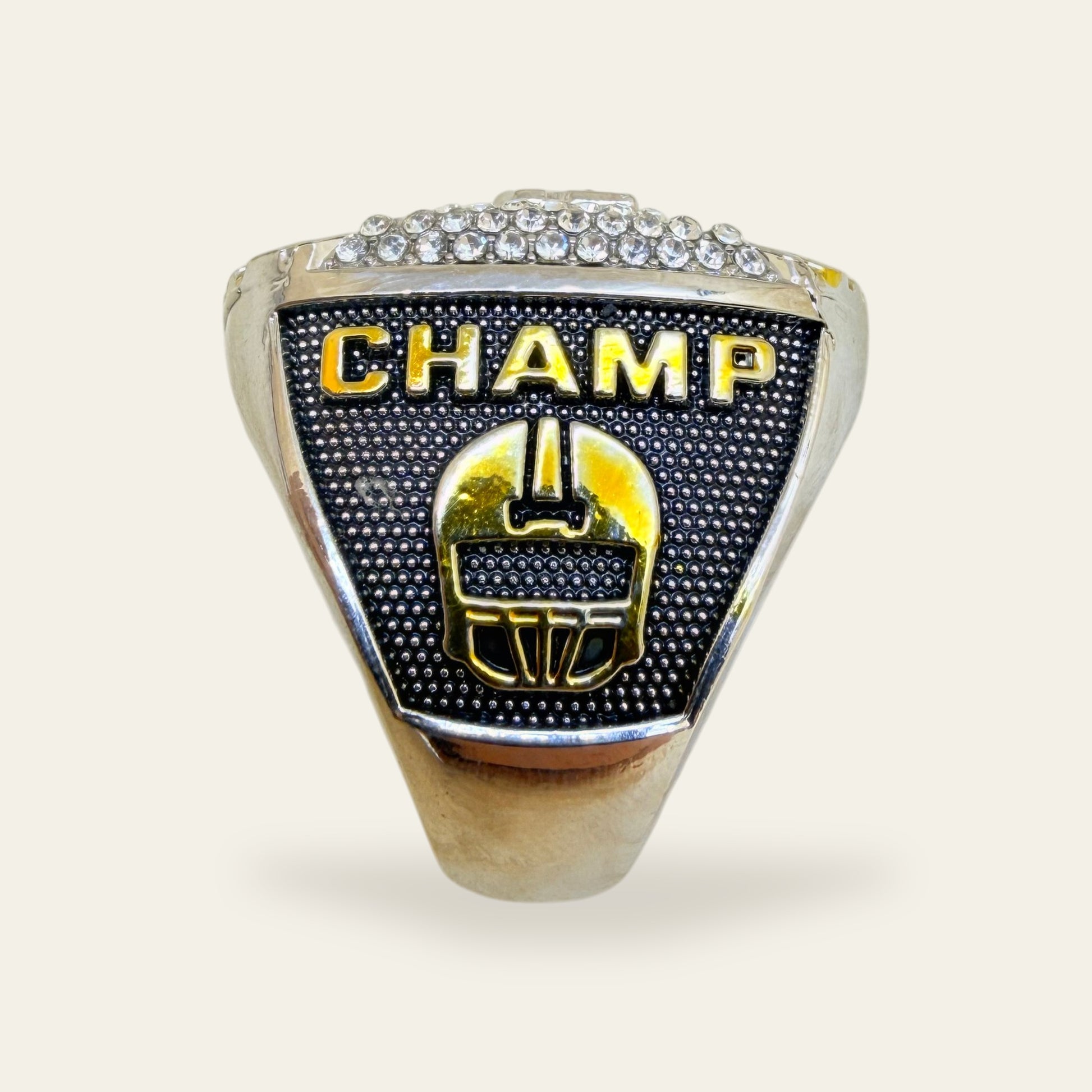 Two tone fantasy football championship ring, left shoulder view, with gold CHAMP letters above a gold football helmet on a black stippled panel, under a row of clear stones.